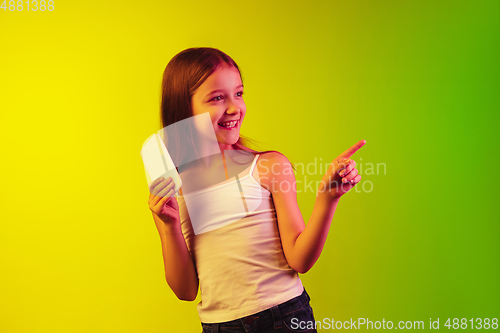 Image of Little caucasian girl\'s portrait isolated on gradient background in neon light. Concept of human emotions, facial expression, modern gadgets and technologies. Copyspace.