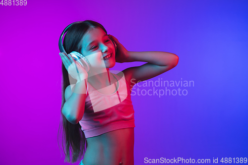 Image of Little caucasian girl\'s portrait isolated on gradient pink-blue background in neon light.