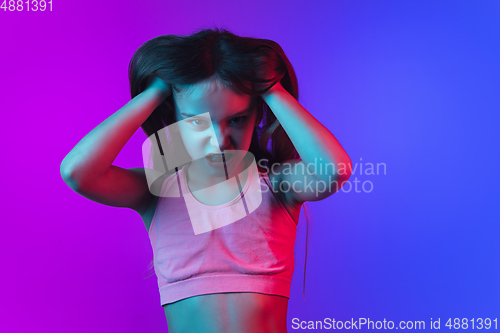 Image of Little caucasian girl\'s portrait isolated on gradient pink-blue background in neon light.