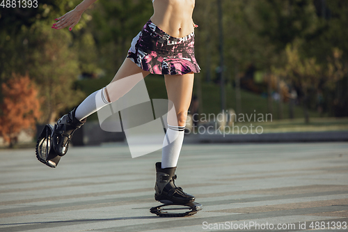Image of Beautiful woman in sportswear jumping in a kangoo jumps shoes at the street on summer\'s sunny day