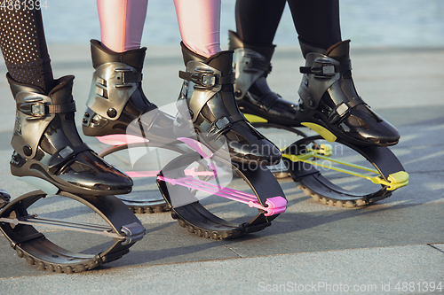 Image of Beautiful women in sportswear jumping in a kangoo jumps shoes at the street on summer\'s sunny day