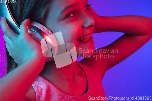 Image of Little caucasian girl\'s portrait isolated on gradient pink-blue background in neon light.