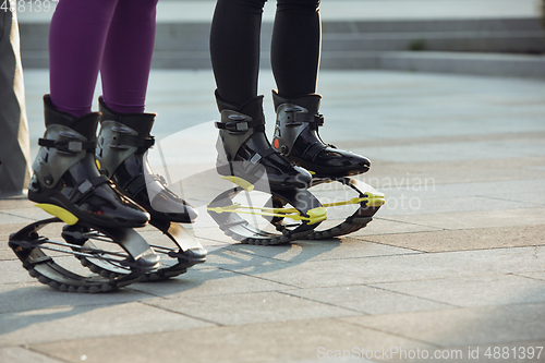 Image of Beautiful women in sportswear jumping in a kangoo jumps shoes at the street on summer\'s sunny day