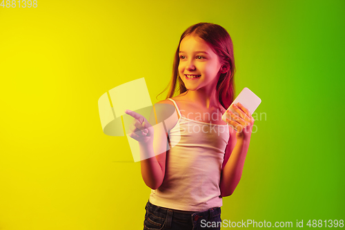 Image of Little caucasian girl\'s portrait isolated on gradient background in neon light. Concept of human emotions, facial expression, modern gadgets and technologies. Copyspace.