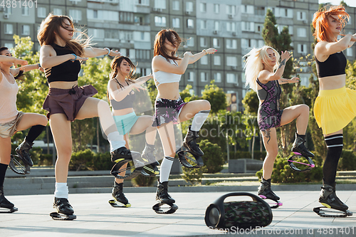 Image of Beautiful women in sportswear jumping in a kangoo jumps shoes at the street on summer\'s sunny day