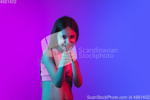 Image of Little caucasian girl\'s portrait isolated on gradient pink-blue background in neon light.