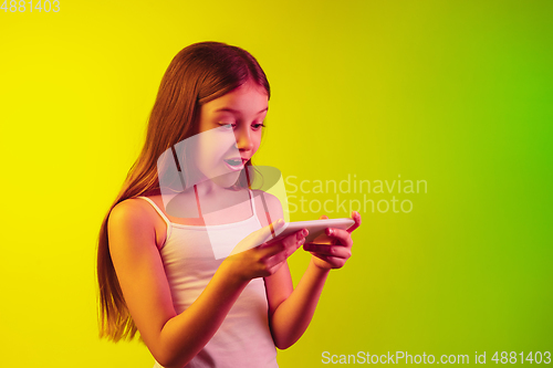 Image of Little caucasian girl\'s portrait isolated on gradient background in neon light. Concept of human emotions, facial expression, modern gadgets and technologies. Copyspace.
