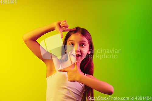 Image of Little caucasian girl\'s portrait isolated on gradient background in neon light. Concept of human emotions, facial expression, modern gadgets and technologies. Copyspace.