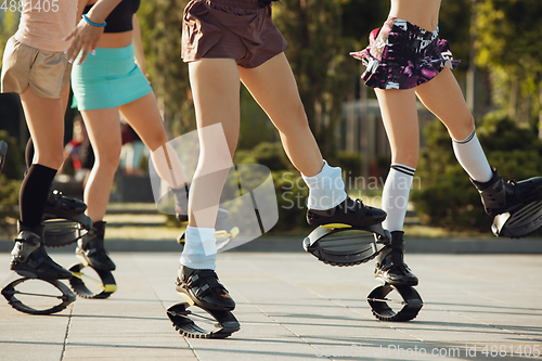 Image of Beautiful women in sportswear jumping in a kangoo jumps shoes at the street on summer\'s sunny day