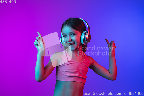Image of Little caucasian girl\'s portrait isolated on gradient pink-blue background in neon light.