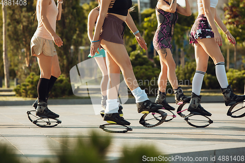 Image of Beautiful women in sportswear jumping in a kangoo jumps shoes at the street on summer\'s sunny day