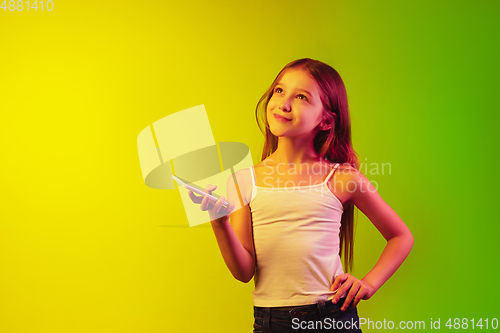 Image of Little caucasian girl\'s portrait isolated on gradient background in neon light. Concept of human emotions, facial expression, modern gadgets and technologies. Copyspace.