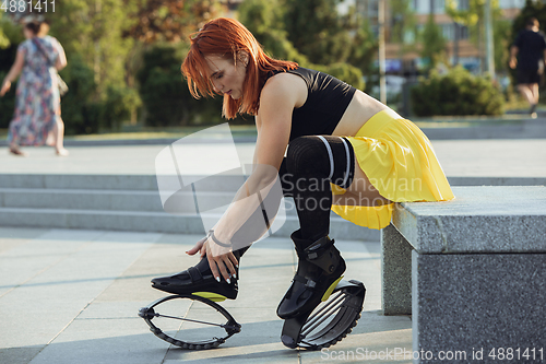 Image of Beautiful woman in sportswear jumping in a kangoo jumps shoes at the street on summer\'s sunny day