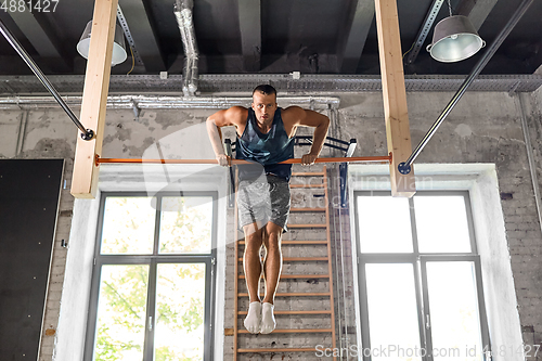 Image of young man exercising on horizontal bar in gym