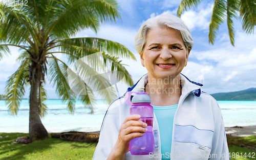 Image of sporty senior woman with bottle of water at park