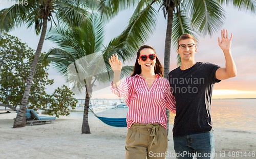 Image of happy couple waving hands on beach