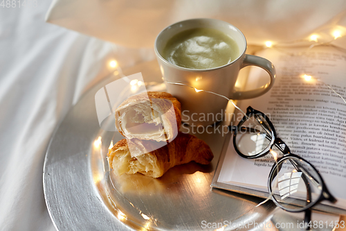 Image of croissants, matcha tea, book and glasses in bed