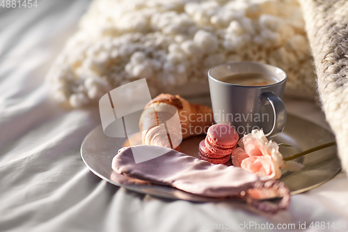 Image of croissant, coffee and eye sleeping mask in bed