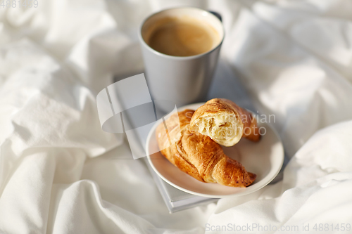 Image of croissants, cup of coffee and book in bed at home