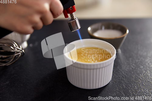 Image of hand with burner making sugar crust in baking dish