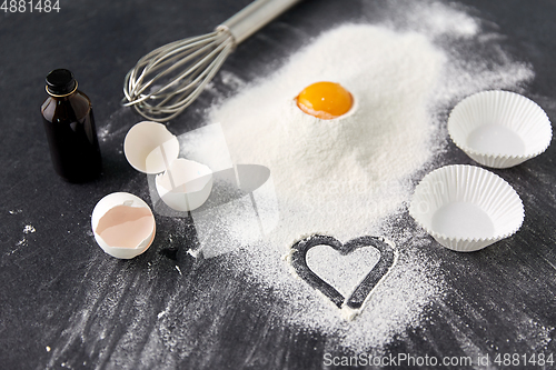 Image of flour, egg, whisk and paper baking molds on table