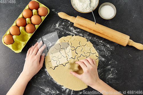 Image of hands cutting dough with star mold on table