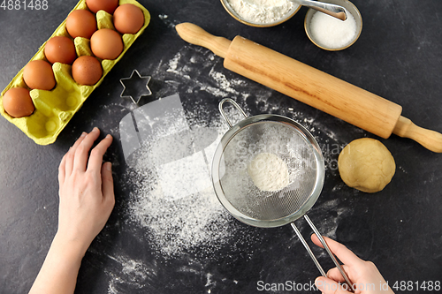 Image of hands with strainer sifting flour on kitchen table