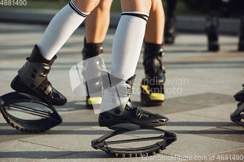 Image of Beautiful women in sportswear jumping in a kangoo jumps shoes at the street on summer\'s sunny day