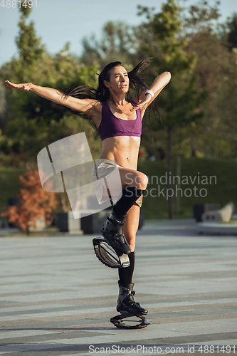 Image of Beautiful woman in sportswear jumping in a kangoo jumps shoes at the street on summer\'s sunny day