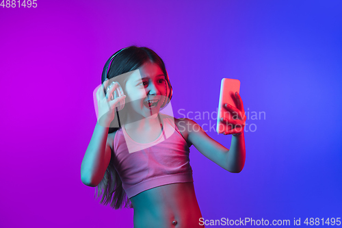 Image of Little caucasian girl\'s portrait isolated on gradient pink-blue background in neon light.