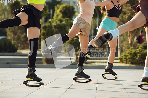 Image of Beautiful women in sportswear jumping in a kangoo jumps shoes at the street on summer\'s sunny day