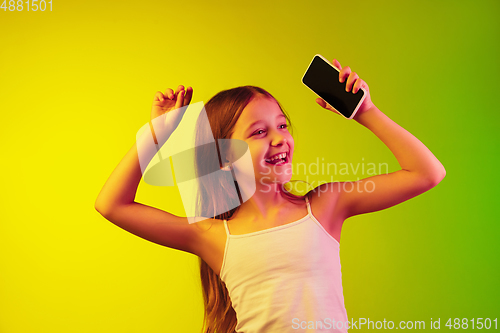 Image of Little caucasian girl\'s portrait isolated on gradient background in neon light. Concept of human emotions, facial expression, modern gadgets and technologies. Copyspace.