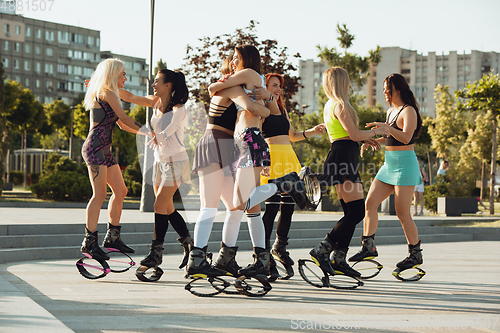 Image of Beautiful women in sportswear jumping in a kangoo jumps shoes at the street on summer\'s sunny day