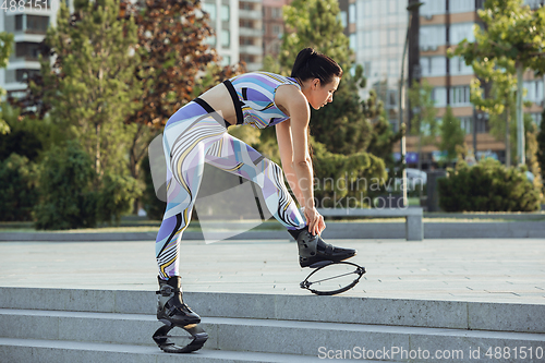 Image of Beautiful woman in sportswear jumping in a kangoo jumps shoes at the street on summer\'s sunny day