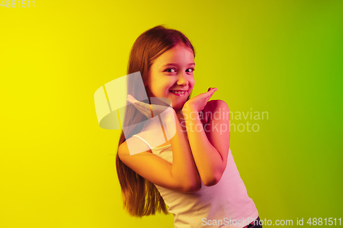 Image of Little caucasian girl\'s portrait isolated on gradient background in neon light. Concept of human emotions, facial expression, modern gadgets and technologies. Copyspace.