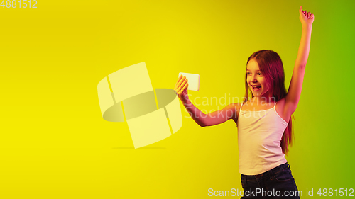 Image of Little caucasian girl\'s portrait isolated on gradient background in neon light. Concept of human emotions, facial expression, modern gadgets and technologies. Copyspace.