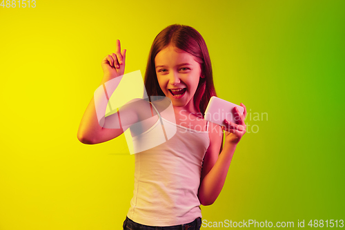 Image of Little caucasian girl\'s portrait isolated on gradient background in neon light. Concept of human emotions, facial expression, modern gadgets and technologies. Copyspace.