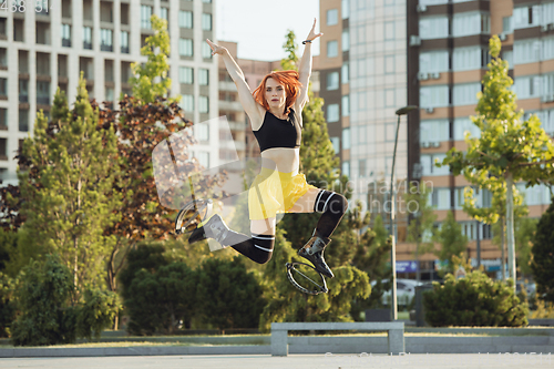 Image of Beautiful woman in sportswear jumping in a kangoo jumps shoes at the street on summer\'s sunny day