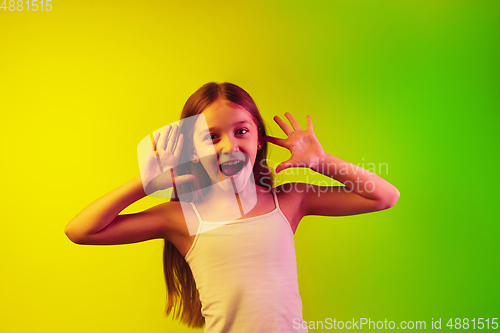 Image of Little caucasian girl\'s portrait isolated on gradient background in neon light. Concept of human emotions, facial expression, modern gadgets and technologies. Copyspace.