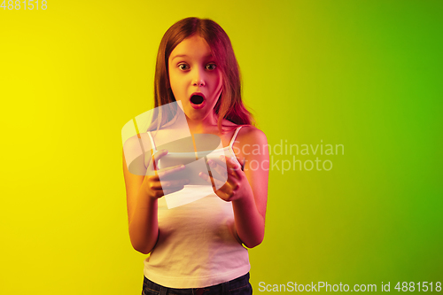 Image of Little caucasian girl\'s portrait isolated on gradient background in neon light. Concept of human emotions, facial expression, modern gadgets and technologies. Copyspace.