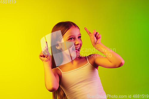 Image of Little caucasian girl\'s portrait isolated on gradient background in neon light. Concept of human emotions, facial expression, modern gadgets and technologies. Copyspace.