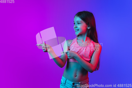 Image of Little caucasian girl\'s portrait isolated on gradient pink-blue background in neon light.