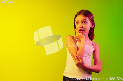 Image of Little caucasian girl\'s portrait isolated on gradient background in neon light. Concept of human emotions, facial expression, modern gadgets and technologies. Copyspace.