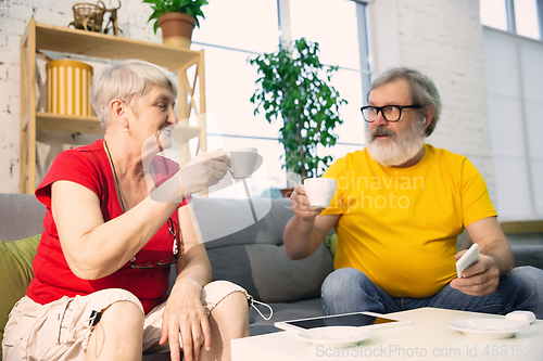 Image of Couple of seniors spending time together being quarantined - caucasians mature and retired man and woman using modern gadgets, talking, drinking tea