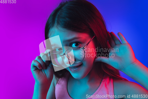 Image of Little caucasian girl\'s portrait isolated on gradient pink-blue background in neon light.