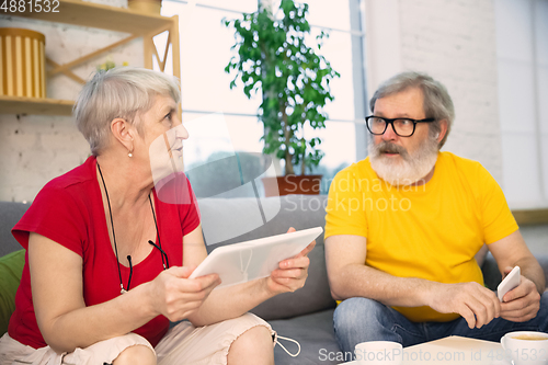 Image of Couple of seniors spending time together being quarantined - caucasians mature and retired man and woman using modern gadgets, talking, drinking tea