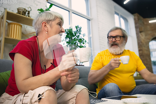 Image of Couple of seniors spending time together being quarantined - caucasians mature and retired man and woman using modern gadgets, talking, drinking tea