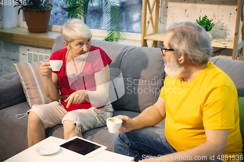 Image of Couple of seniors spending time together being quarantined - caucasians mature and retired man and woman using modern gadgets, talking, drinking tea
