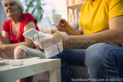 Image of Couple of seniors spending time together being quarantined - caucasians mature and retired man and woman using modern gadgets, talking, drinking tea