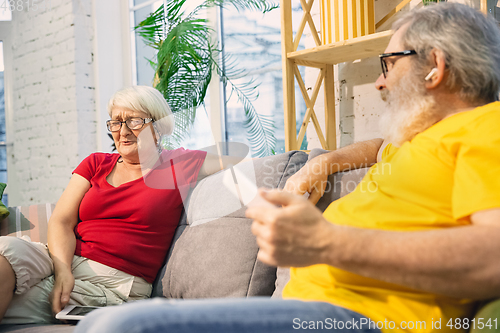 Image of Couple of seniors spending time together being quarantined - caucasians mature and retired man and woman using modern gadgets, talking, drinking tea